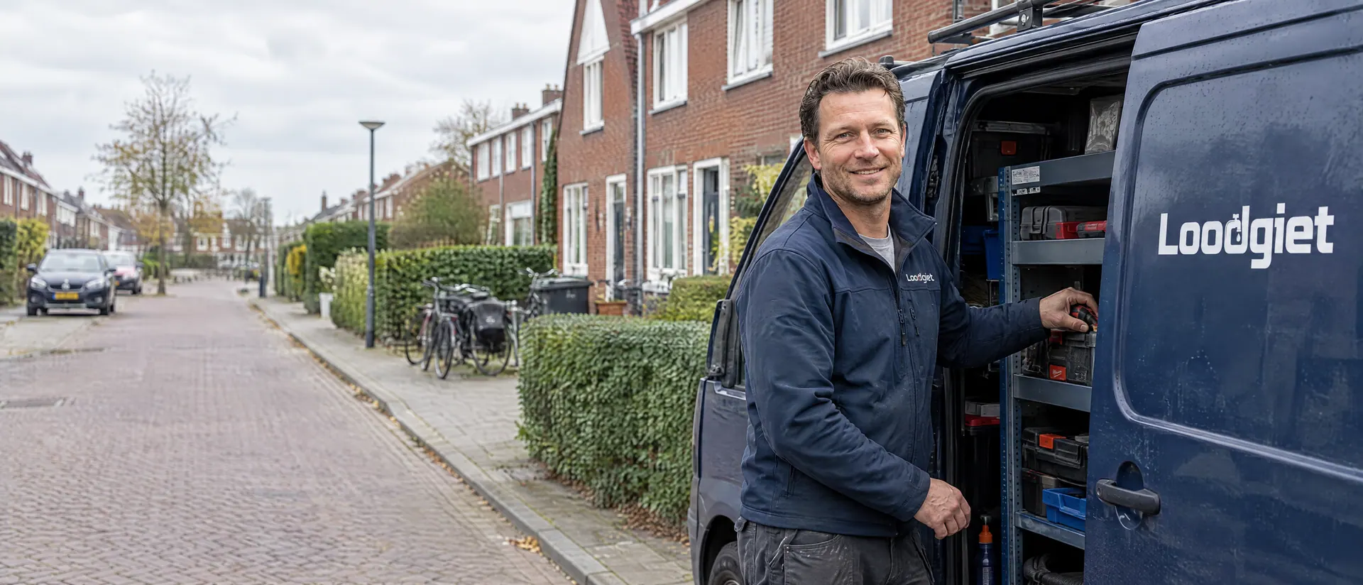 Monteur van Loodgiet bij de open zijdeur van de Loodgiet-bus, in een rustige woonstraat